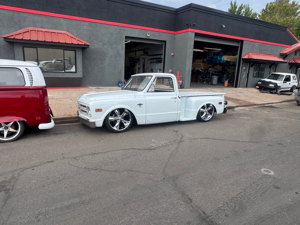Wide daylight view of the white 1968 Chevrolet C10 Stepside parked outside a workshop.