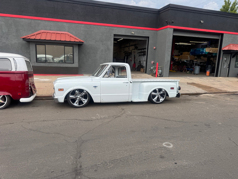 Wide side-profile photograph of the white 1968 Chevrolet C10 Stepside outside a workshop.