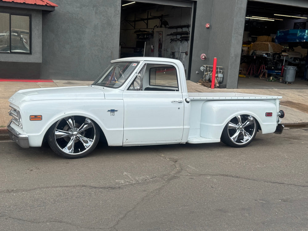 Close side profile of the white 1968 Chevrolet C10 Stepside, showing chrome wheels, cab, door and stepside bed.