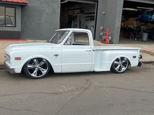 Close side profile of the white 1968 Chevrolet C10 Stepside, showing chrome wheels, cab, door and stepside bed.